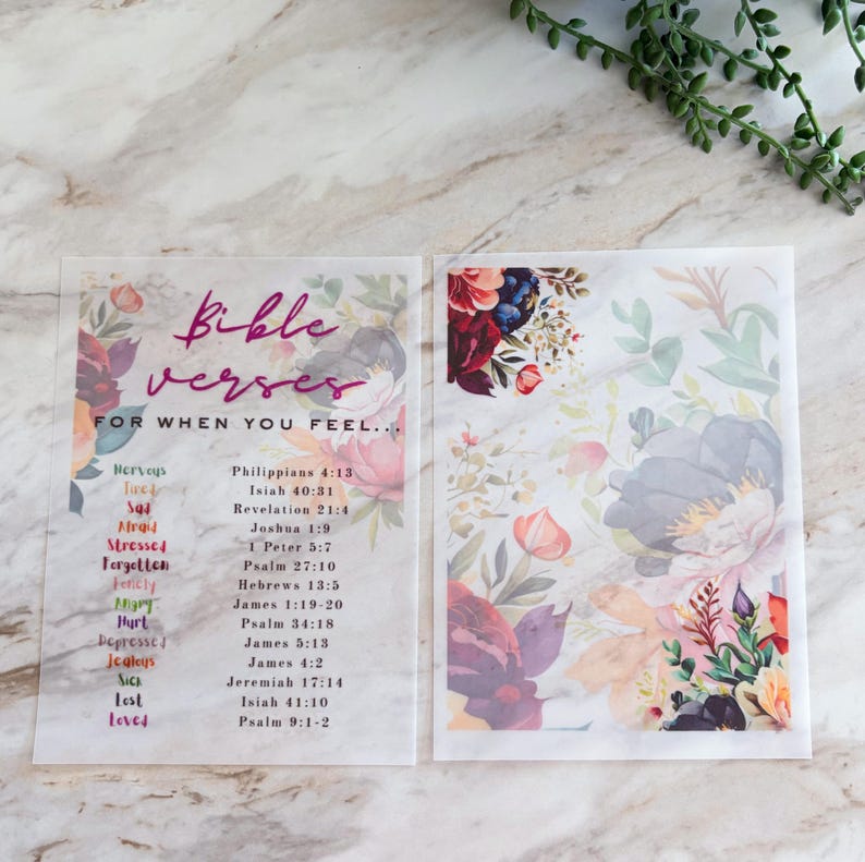 May include: Two translucent rectangular sheets featuring floral illustrations and text. The left sheet displays the title Bible verses for when you feel... followed by a list of emotions and corresponding scripture references. The right sheet features a floral design.