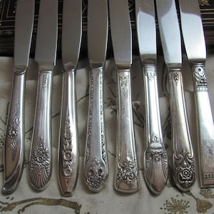 May include: Eight silver dinner knives with ornate handles. The knives have a polished finish and intricate floral designs.