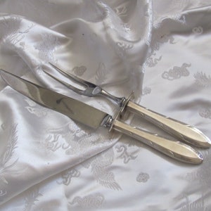 Può includere: Un set da intaglio in argento con coltello e forchetta. Il set ha un design semplice ed elegante con un manico leggermente curvo.