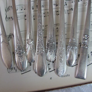 May include: Eight silver-plated forks with ornate designs on the handles. The forks are arranged in a row on a sheet of music.