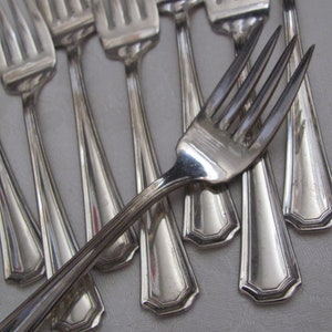 Puede incluir: Un juego de tenedores de plata con mangos ornamentados. Los tenedores están dispuestos en forma de abanico, con los dientes de los tenedores apuntando hacia la parte superior de la imagen.