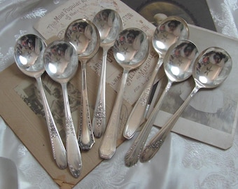 May include: A set of eight silver-plated soup spoons with ornate handles. The spoons are arranged on a vintage postcard with text that reads "The Most Popular Articles of their kind".