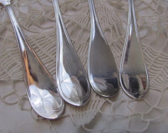 Può includere: Quattro forchette d'argento con decorazioni elaborate sui manici, appoggiate su una superficie di uncinetto bianca.