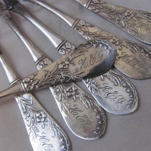 Puede incluir: Juego de seis cuchillos de mantequilla de plata con diseños florales ornamentados y las iniciales "H. & F." grabadas en cada hoja.