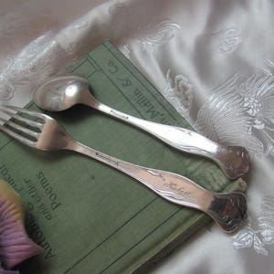 May include: A silver fork and spoon with engraved names "Robert" and "Annemarie". The silverware is resting on a green book with the title "Anthology of Poems and Other Treat".