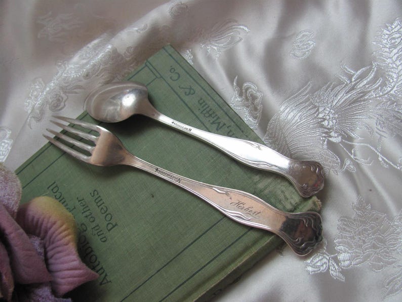May include: A silver fork and spoon with engraved names "Robert" and "Annemarie". The silverware is resting on a green book with the title "Anthology of Poems and Other Treat".