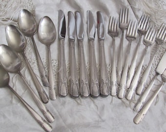 Op de afbeelding: Een set bestek, inclusief lepels, vorken en een botermes, allemaal met sierlijke ontwerpen. Het bestek is gemaakt van gepolijst zilver en heeft een vintage uitstraling.