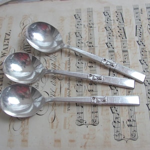 May include: Three silver spoons with ornate handles rest on a vintage sheet music background. The spoons have a rounded bowl and a decorative design on the handle. The sheet music has text that reads "THE HUNGARIAN WALTZ".