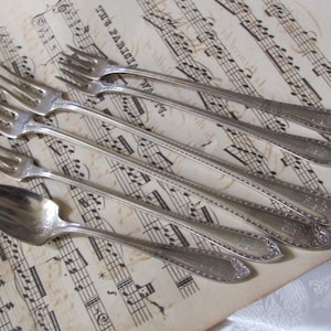 May include: Set of six silver-plated forks with ornate handles. The forks are arranged on a sheet of music.