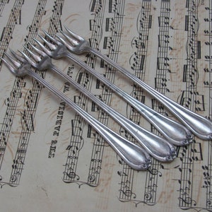 May include: Four silver forks with ornate handles, lying on a sheet of music with black printed notes.