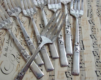 May include: A collection of antique silver forks with ornate floral detailing on the handles. The forks are arranged on a vintage sheet music background, creating a classic and elegant aesthetic. The tines of the forks are visible.