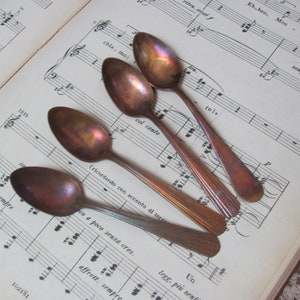 May include: Four antique copper spoons with a worn, aged patina. The spoons are arranged on a sheet of music with musical notes and Italian text.
