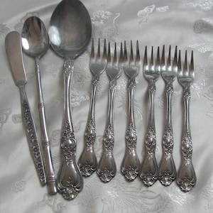 May include: A set of silverware with ornate handles, including a butter knife, a spoon, a serving spoon, and eight forks.