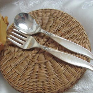 May include: A silver fork and spoon set on a woven placemat. The fork and spoon have ornate designs.