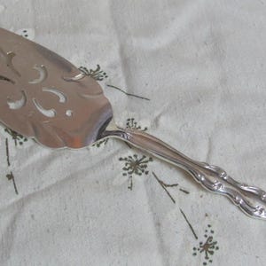 Può includere: Un servizio per torta d'argento con un design ornamentale. Il servizio ha un manico decorativo e un bordo smerlato.