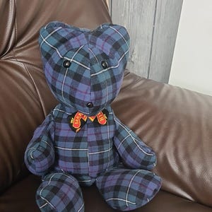 May include: A blue and black plaid teddy bear with a red and yellow bow tie. The bow tie has the words "Manchester" on it.