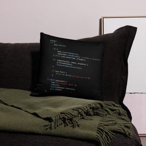May include: Black cushion featuring a printed code snippet in white and red text. The code includes phrases like "try your best()", "celebrateSmallVictories()", and "throw new Worry". The cushion is on a dark sofa with a green blanket.