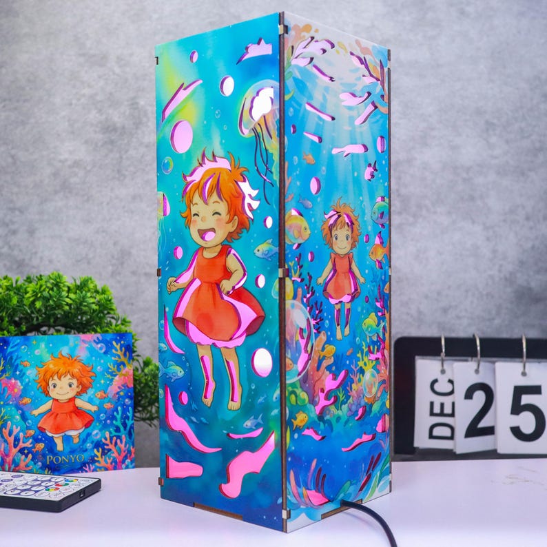 May include: A rectangular lamp featuring a vibrant underwater scene with a cartoon character in a red dress, jellyfish, and colorful coral. The design includes blue water tones and bubbles, with a matching square print and a remote control nearby.
