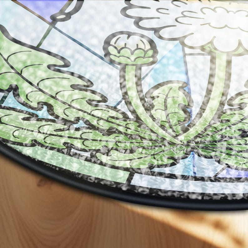 May include: Round decorative rug with a floral design. The rug features a detailed illustration of green leaves and flower buds with black outlines, set against a backdrop of light blue and white. The rug has a black border and is placed on a wooden surface.