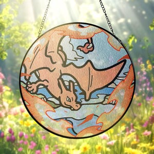 Puede incluir: Vidriera redonda con un diseño de Charizard. La obra de arte representa al Pokémon en naranja y negro, rodeado de llamas y sobre un fondo azul y blanco. La ventana está suspendida por una cadena.