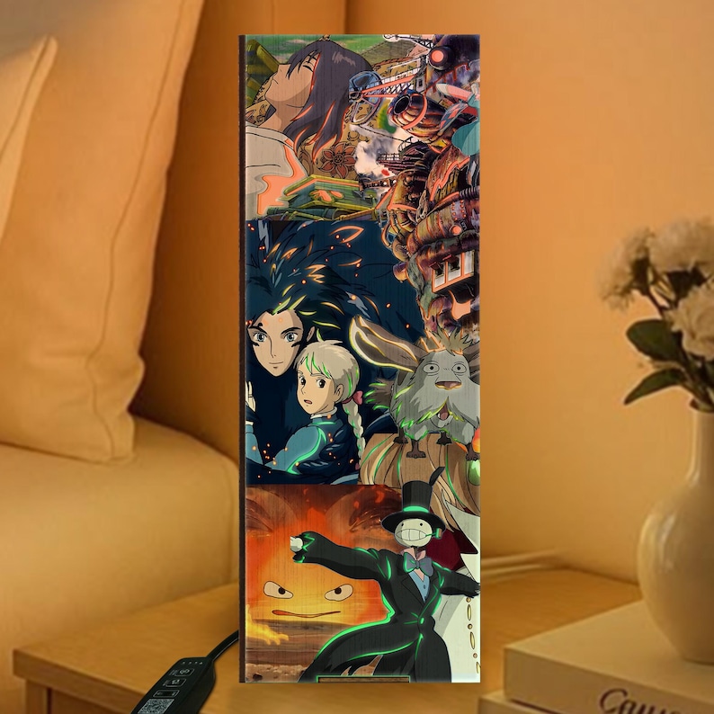 K&ouml;nnte beinhalten: Rechteckige Holzlampe mit einer Collage von Anime-Charakteren und -Szenen. Das Kunstwerk zeigt Charaktere mit langen Haaren, ein junges M&auml;dchen und eine Figur in einem schwarzen Anzug. Die Lampe ist beleuchtet und strahlt ein warmes Licht aus.
