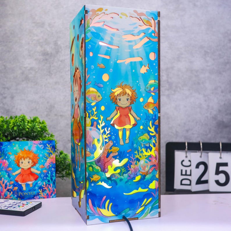 May include: A rectangular lamp featuring a vibrant underwater scene with a cartoon character in a red dress swimming among colorful coral, fish, and bubbles. The design includes light blue water tones and a matching square print on the side.