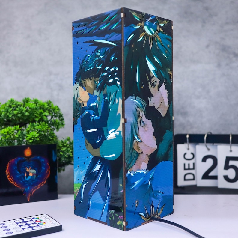 May include: A rectangular wooden lamp featuring a blue and teal anime-style illustration of two couples embracing. The lamp has a black power cord and is next to a remote control and a calendar showing December 25.