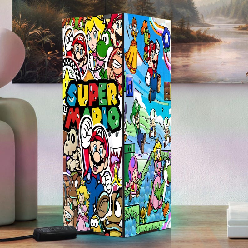 Puede incluir: Una l&aacute;mpara rectangular con un colorido collage de personajes de Super Mario y el logotipo del juego. El dise&ntilde;o de la l&aacute;mpara incluye a Mario, Luigi, la Princesa Peach y otros personajes ic&oacute;nicos. La l&aacute;mpara est&aacute; sobre una superficie de madera.