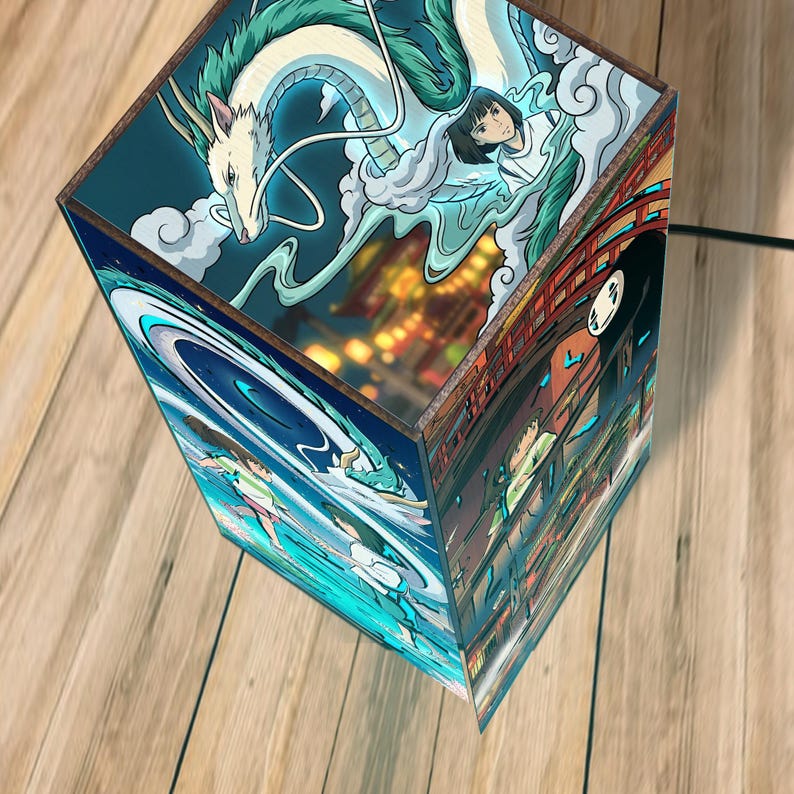 Puede incluir: L&aacute;mpara c&uacute;bica decorativa con ilustraciones de una pel&iacute;cula de animaci&oacute;n. Los lados de la l&aacute;mpara muestran ilustraciones coloridas de un drag&oacute;n, una ni&ntilde;a y otros personajes. La l&aacute;mpara es de madera y emite una luz c&aacute;lida.