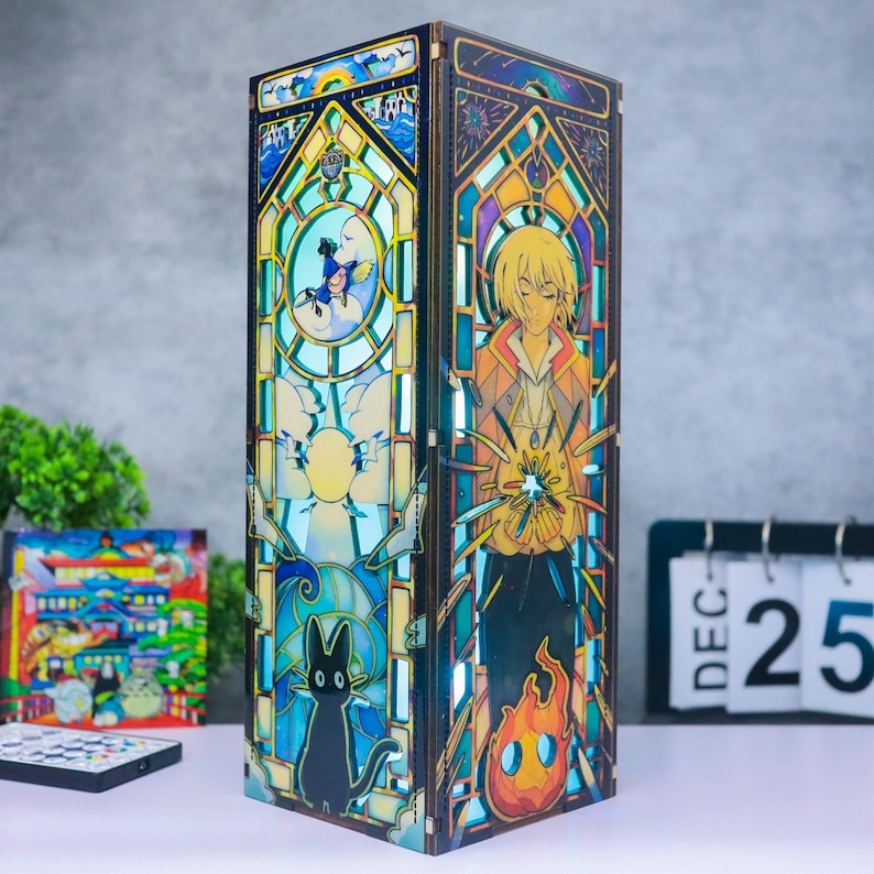 May include: A rectangular wooden lamp featuring intricate stained glass-style panels. One side displays a blonde character with a fire spirit, while the other shows a black cat and a small blue figure. The panels are illuminated with blue and yellow light.