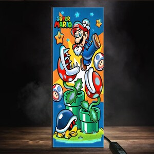 Puede incluir: Panel vertical con una ilustraci&oacute;n de Super Mario. La obra muestra a Mario saltando, junto con estrellas, champi&ntilde;ones y plantas Pira&ntilde;a, sobre un fondo azul y naranja. Las palabras "SUPER MARIO" est&aacute;n en la parte superior. El panel es rectangular.