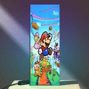 Puede incluir: L&aacute;mpara rectangular con una colorida ilustraci&oacute;n de personajes de la serie de videojuegos Super Mario. El dise&ntilde;o incluye a Mario, la Princesa Peach, Bowser y Luigi, sobre un fondo vibrante y estilizado con plataformas flotantes y un cielo azul.