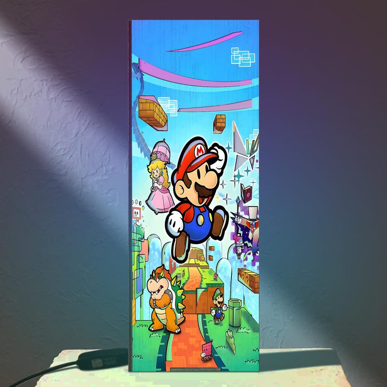 Puede incluir: L&aacute;mpara rectangular con una colorida ilustraci&oacute;n de personajes de la serie de videojuegos Super Mario. El dise&ntilde;o incluye a Mario, la Princesa Peach, Bowser y Luigi, sobre un fondo vibrante y estilizado con plataformas flotantes y un cielo azul.
