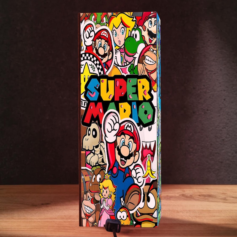Puede incluir: Una caja rectangular cubierta de pegatinas coloridas con personajes de Super Mario. El texto "SUPER MARIO" se muestra de forma destacada en una fuente vibrante y multicolor. La caja est&aacute; sobre una superficie de madera con un fondo oscuro.