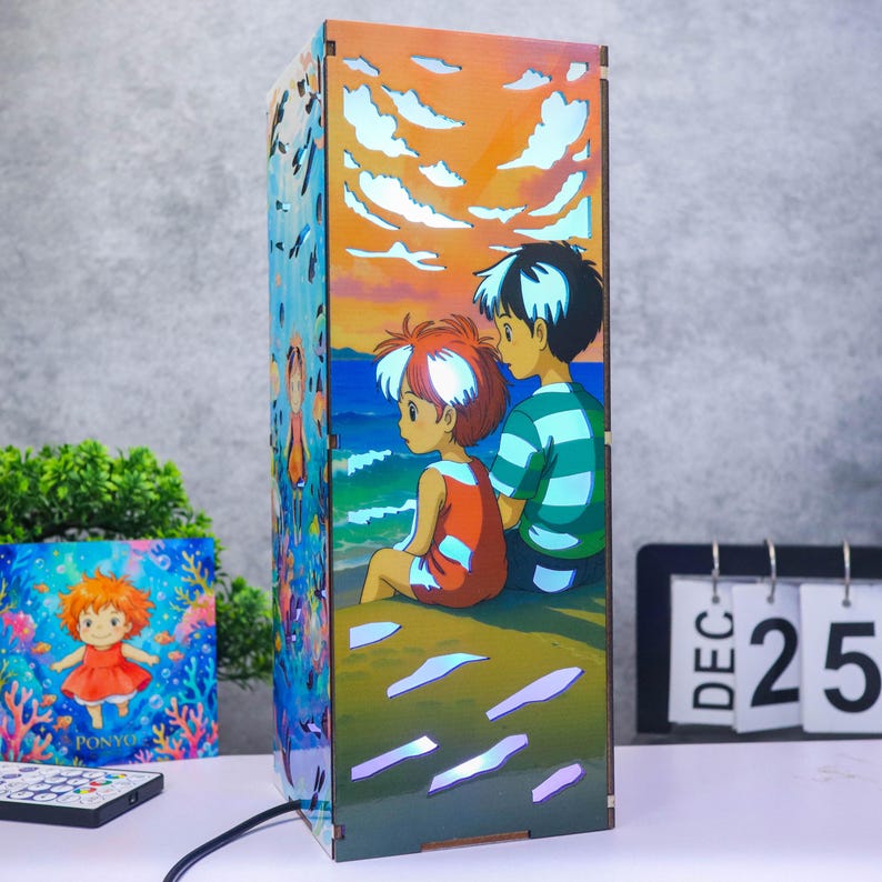 May include: A rectangular wooden lamp featuring a colorful illustration of two animated characters sitting on a beach at sunset. The side panel displays a scene of a small character underwater surrounded by coral and fish with the text PONYO.