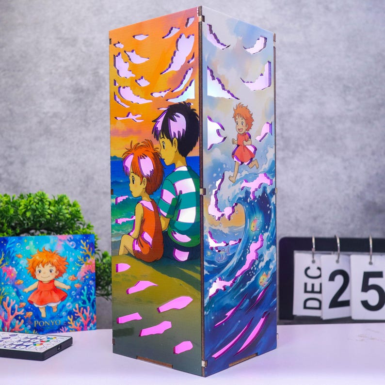 May include: A rectangular wooden lamp featuring colorful anime-style illustrations of characters from Ponyo. One side shows two figures sitting on a beach at sunset, while the other depicts a character running on a wave. The lamp has laser-cut openings.
