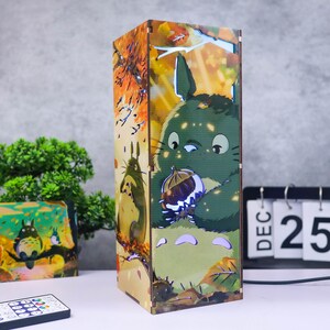Puede incluir: L&aacute;mpara rectangular de madera con un personaje de dibujos animados verde sosteniendo una nuez, con un fondo de escena de bosque. La l&aacute;mpara tiene un mando a distancia y un calendario que muestra el 25 de diciembre.