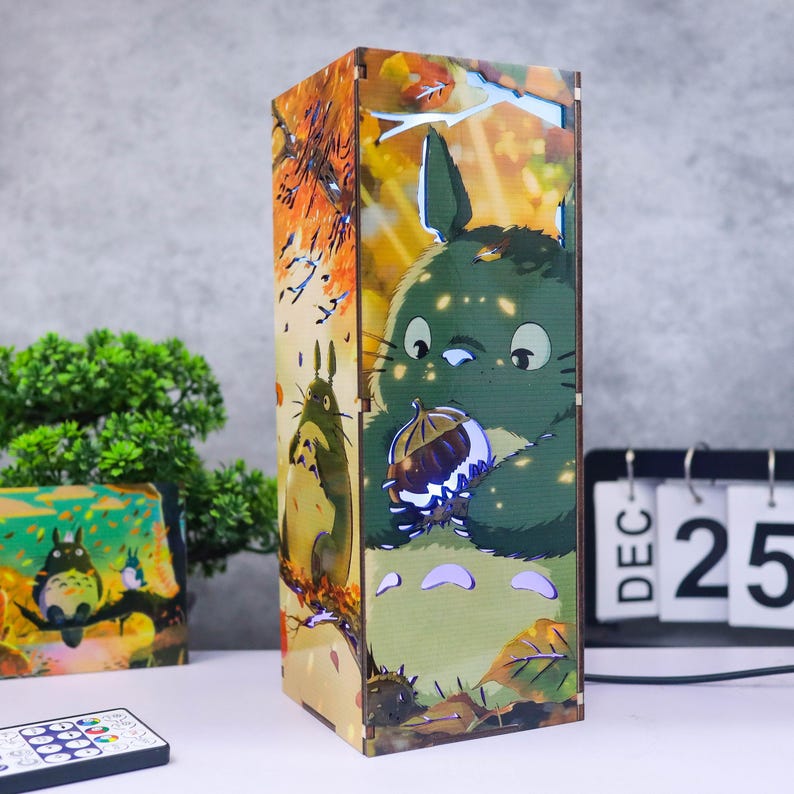 Puede incluir: L&aacute;mpara rectangular de madera con un personaje de dibujos animados verde sosteniendo una nuez, con un fondo de escena de bosque. La l&aacute;mpara tiene un mando a distancia y un calendario que muestra el 25 de diciembre.