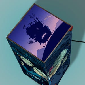May include: A cube-shaped lamp featuring artwork from an animated film. The top of the lamp displays a dark silhouette of a castle against a purple and blue sky. The sides of the lamp depict characters in a blue and dark blue setting.