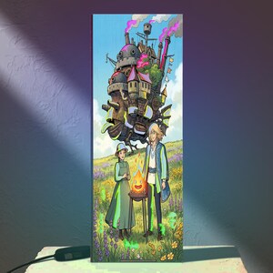 May include: A rectangular vertical light panel featuring a colorful illustration of a large, complex mechanical castle floating above a grassy field with two figures standing near a small, glowing orange fire spirit in a metal cooking stand.