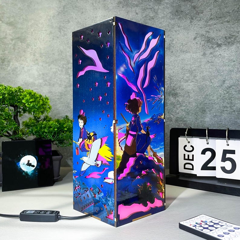 May include: A rectangular lamp with a vibrant anime-style design. The lamp features a blue background with pink and purple accents, and illustrations of characters and scenery. The lamp is plugged in and has a remote control.