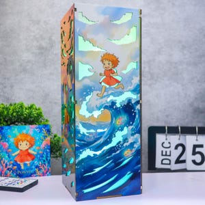 May include: A rectangular light box featuring a colorful illustration of a character with orange hair in a red dress running across ocean waves. The design includes cut-out cloud shapes that emit a soft light, with fish swimming in the blue water.