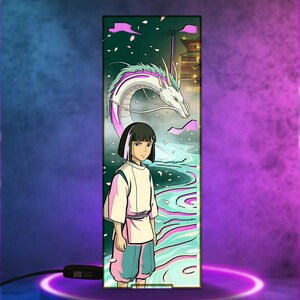 Puede incluir: L&aacute;mpara decorativa con una ilustraci&oacute;n de estilo anime. La obra de arte representa a un joven con un atuendo blanco y rosa, un drag&oacute;n blanco y un edificio tradicional. La l&aacute;mpara es rectangular con una base negra. El fondo es verde y azul.