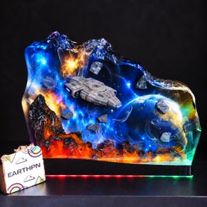 May include: A resin diorama featuring a miniature USS Defiant starship navigating through a space scene with a glowing blue planet, orange nebula clouds, and scattered dark asteroids. The base includes a small sign labeled EARTHPN.