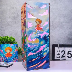 May include: A rectangular wooden lamp featuring a colorful illustration of a character with orange hair running across ocean waves. The design includes cut-out cloud shapes that emit a soft pink light, with dark edges and a vertical orientation.