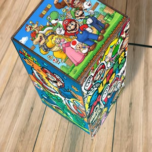 Puede incluir: L&aacute;mpara rectangular con marco de madera, decorada con ilustraciones coloridas de personajes de Super Mario. La l&aacute;mpara presenta im&aacute;genes de Mario, Luigi, la Princesa Peach y otros personajes de la serie de videojuegos.