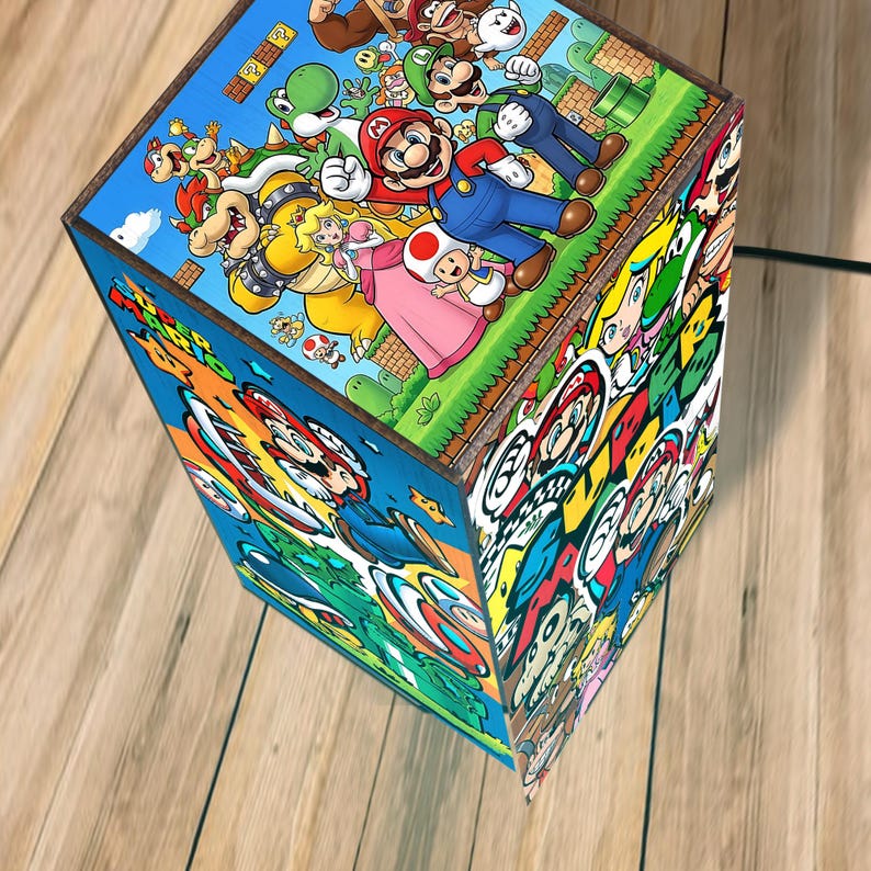 Puede incluir: L&aacute;mpara rectangular con marco de madera, decorada con ilustraciones coloridas de personajes de Super Mario. La l&aacute;mpara presenta im&aacute;genes de Mario, Luigi, la Princesa Peach y otros personajes de la serie de videojuegos.