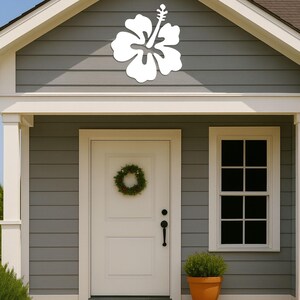 Puede incluir: Una decoraci&oacute;n de flor de hibisco blanca montada en el revestimiento gris de una casa. La casa tiene una puerta blanca con una corona, una ventana y una peque&ntilde;a planta en maceta. Los escalones y los adornos son de madera clara.