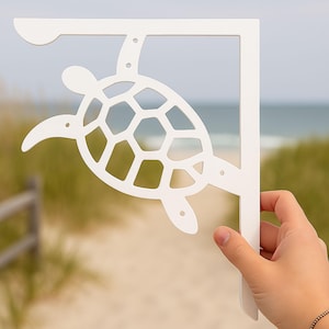 May include: White metal shelf bracket with a cutout of a sea turtle. The bracket is designed to be mounted on a wall.
