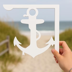 Könnte beinhalten: Weiße Wanddekoration in Ankerform, vor einem Strandhintergrund gehalten. Der Anker ist Teil einer Eckhalterung. Das Design ist aus einem festen Material geschnitten, geeignet für die Wandmontage.